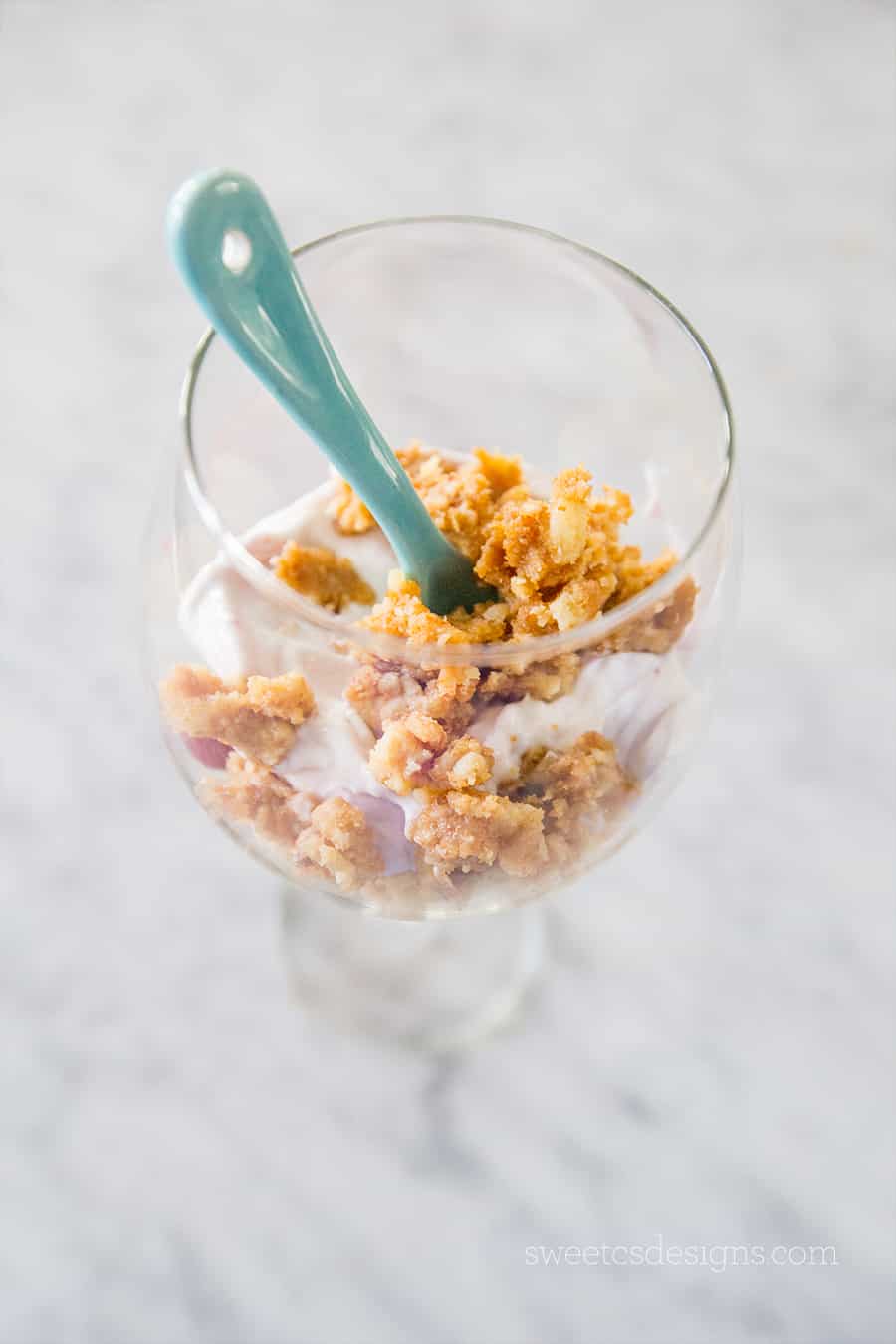 picture of leftovers in a wine glass with yogurt and granola clusters with blue spoon in it. 