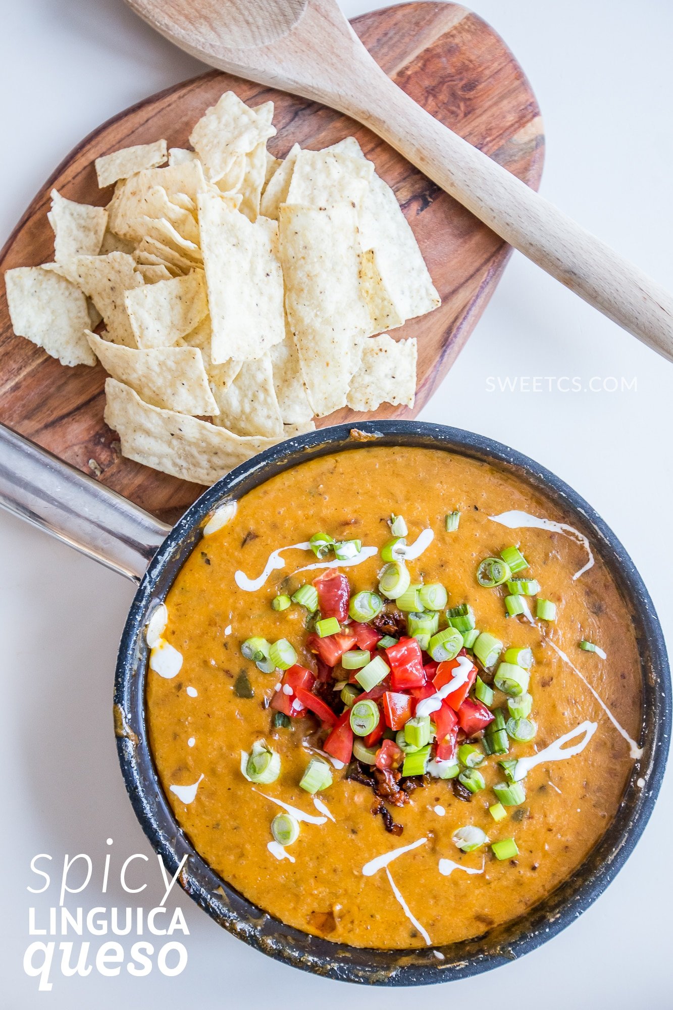 bowl of spicy dip with chiles, peppers, green onions, and creme on the top. Chips on the side and a spoon