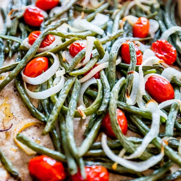 Roasted green beans and tomatoes on a baking sheet for a refreshing salad.