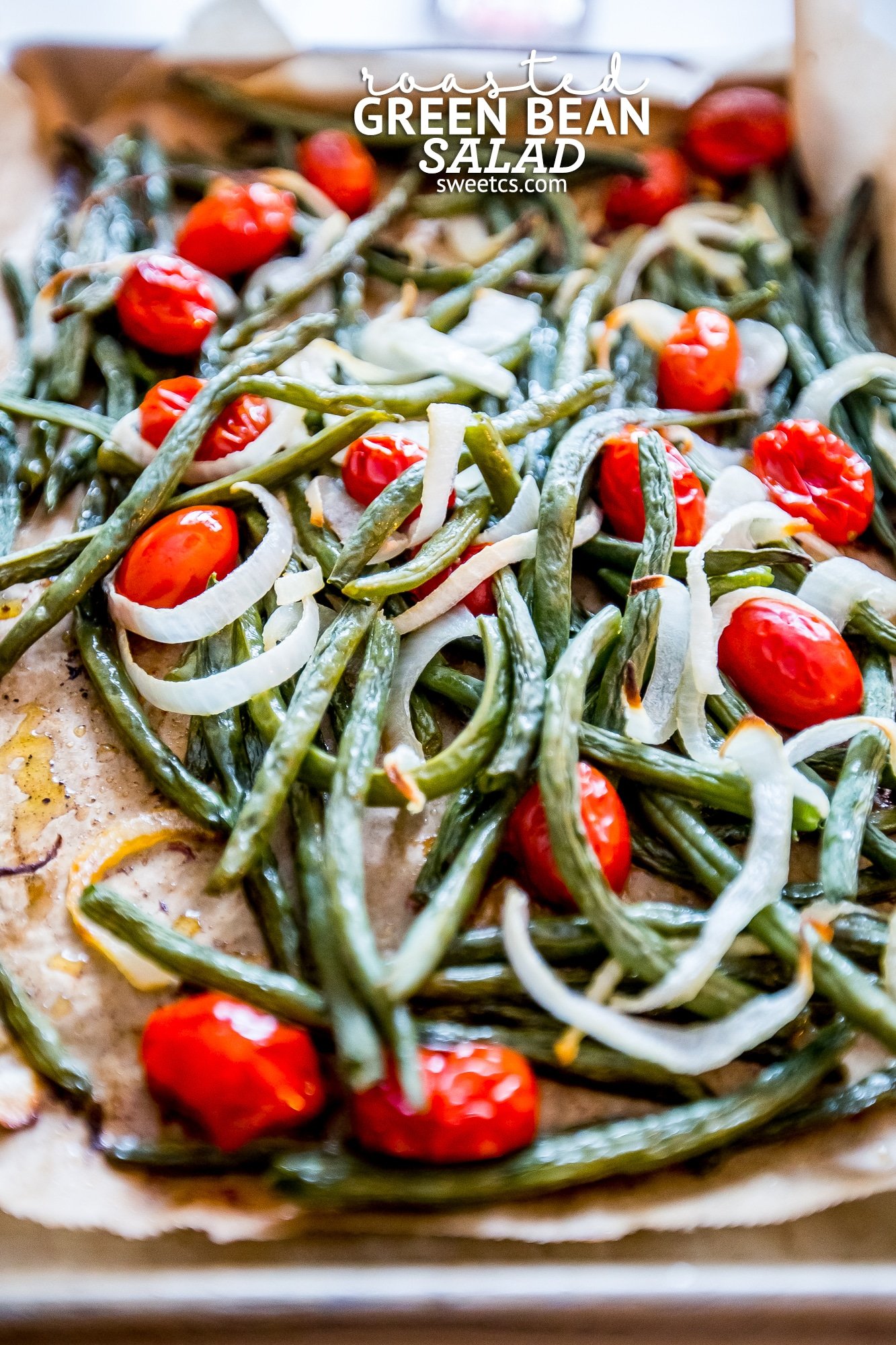 roasted green beans, tomatoes, and onions on parchment paper in a roasting pan