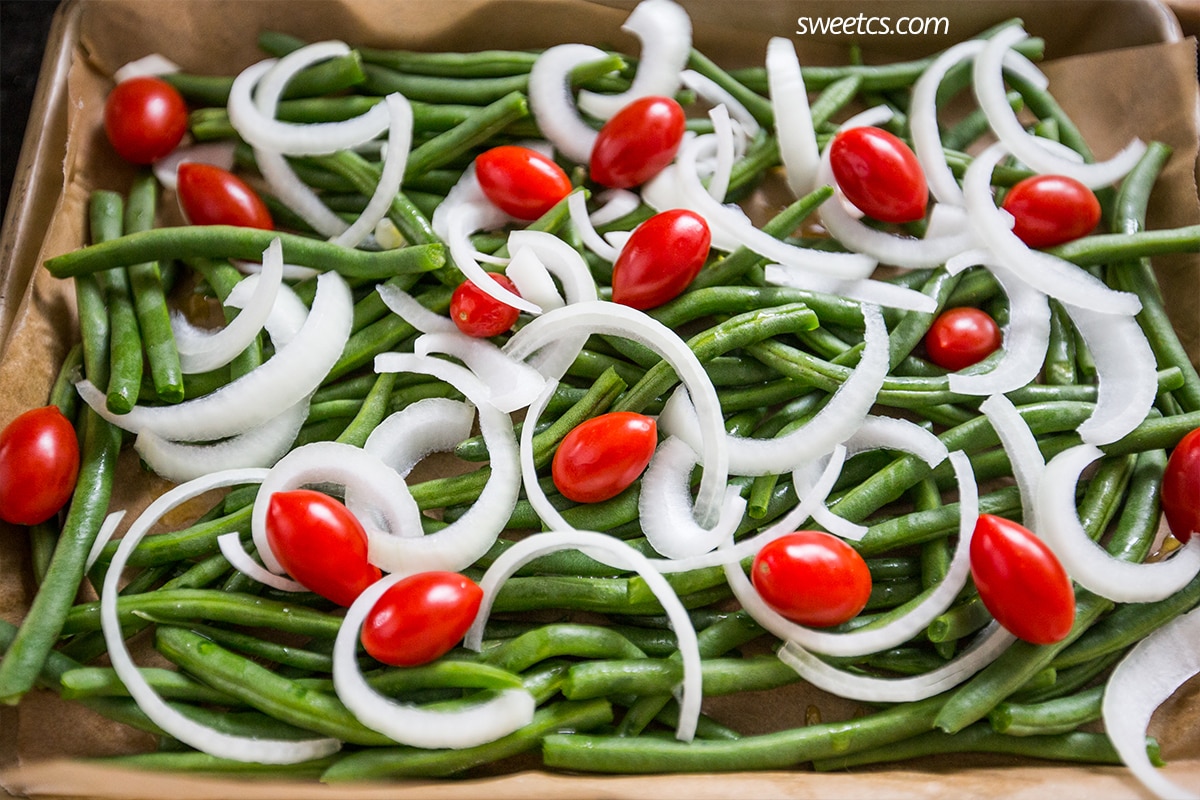 roasted green beans, tomatoes, and onions on parchment paper in a roasting pan