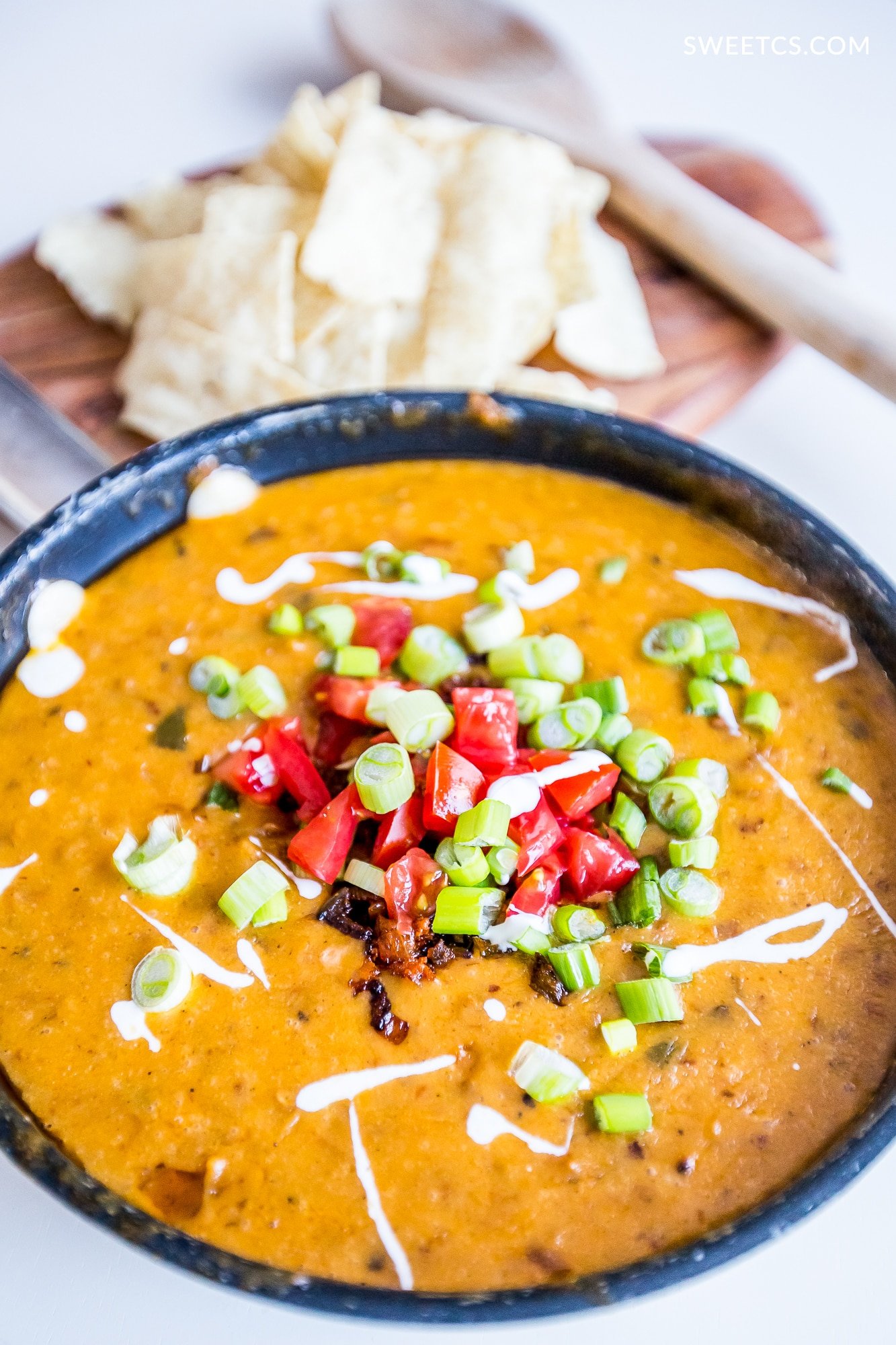 bowl of spicy dip with chiles, peppers, green onions, and creme on the top. Chips on the side and a spoon