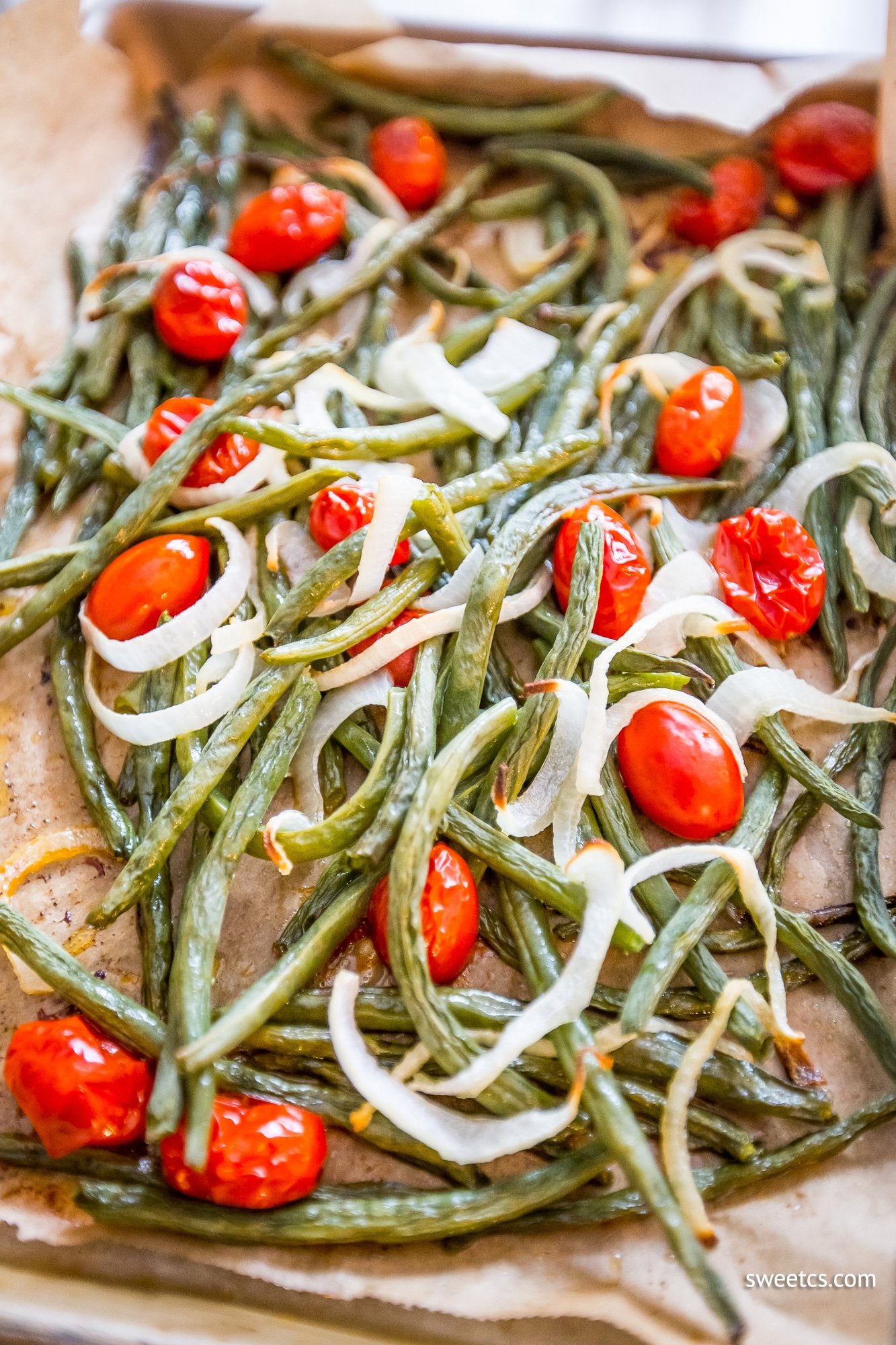 roasted green beans, tomatoes, and onions on parchment paper in a roasting pan