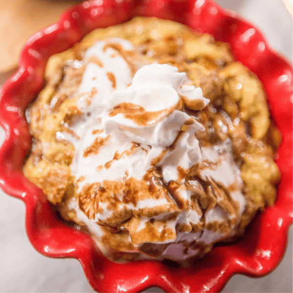 A delightful dessert in a red dish featuring a luscious coffee-soaked bread pudding, finished with whipped cream and a decadent chocolate drizzle.