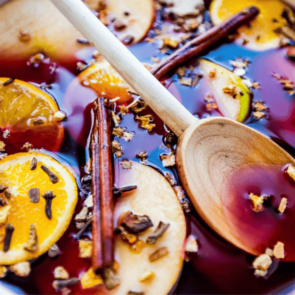 A pot of non-alcoholic ginger wassail, infused with sliced oranges and apples, cinnamon sticks, and cloves, stirred gently with a wooden spoon.