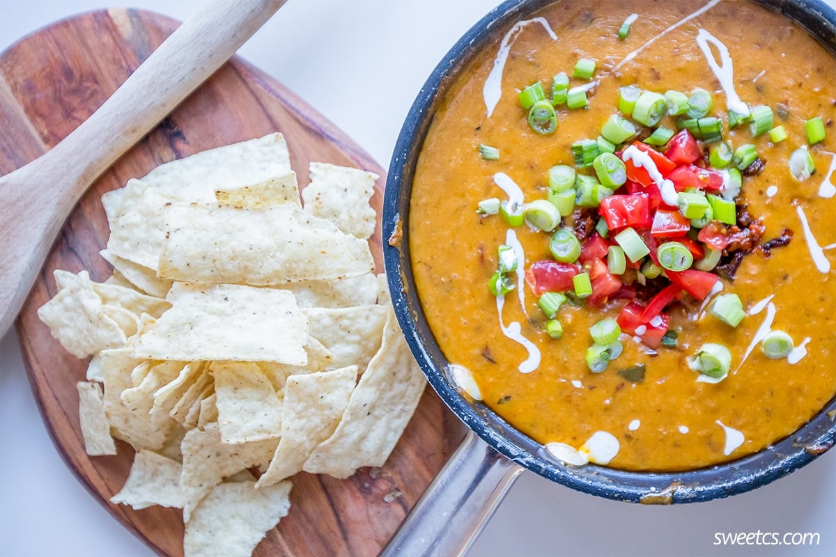 bowl of spicy dip with chiles, peppers, green onions, and creme on the top. Chips on the side and a spoon