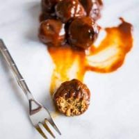 A plate of BBQ meatballs with sauce and a fork.