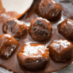 Paleo meatballs simmer in a rich, glossy sauce in a pan. A wooden spoon is slightly visible at the top.