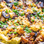 Cheesy scrambled eggs with mushrooms and onions in a skillet.