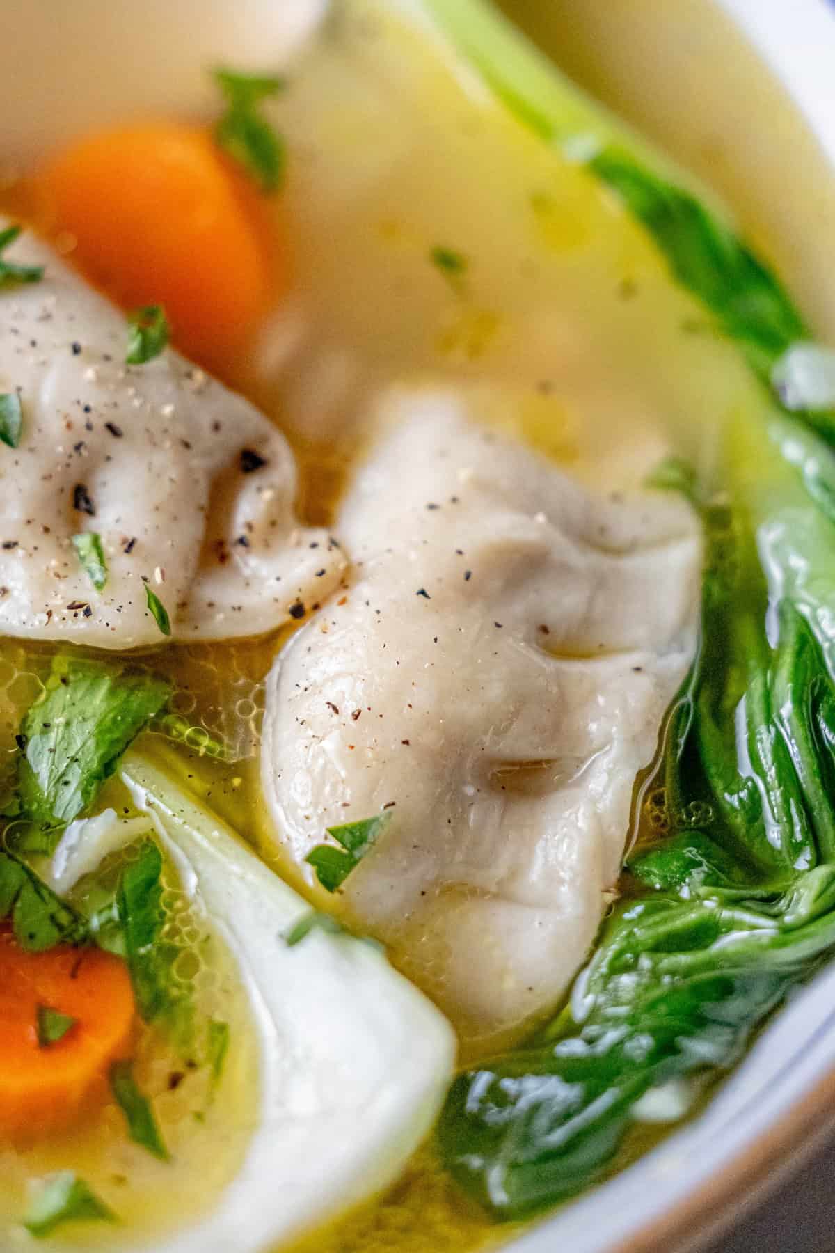 A close-up of a bowl highlights this 15-minute potsticker soup, featuring two dumplings, bok choy, carrot slices, and herbs in a clear broth.