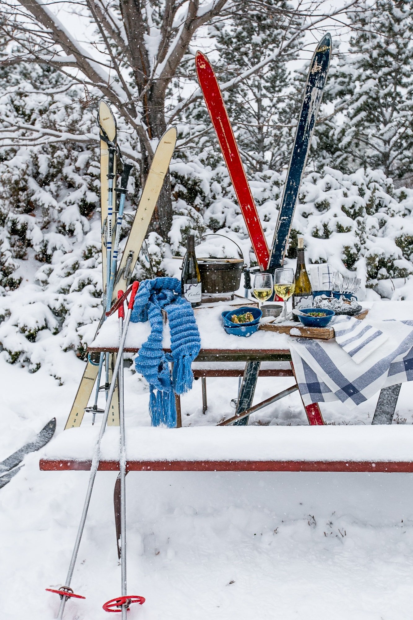 snow covered table with Cambria wine, country rib stuffed potatoes in bowls and skies in the background