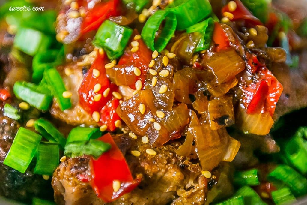 up close picture of asian ribs with sesame seeds and green onions picked up with chop sticks