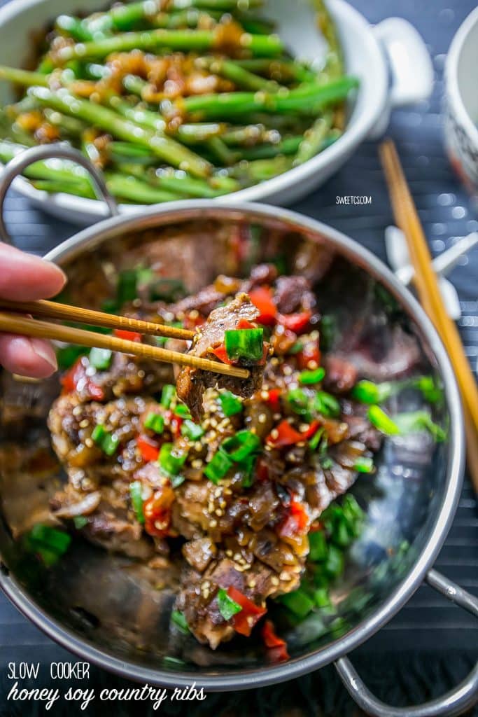 asian ribs with sesame seeds and green onions picked up with chop sticks