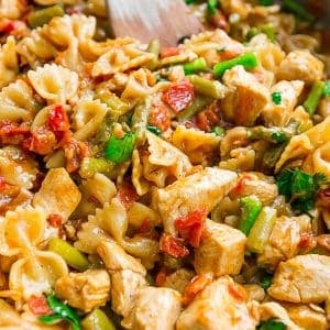 One Pot Bruschetta Chicken Pasta cooked in a pan with a wooden spoon.