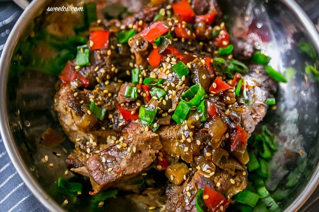 asian ribs with sesame seeds and green onions and veggies in a metal bowl. 