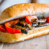 A vegan hoagie with mushrooms and peppers on a wooden board.