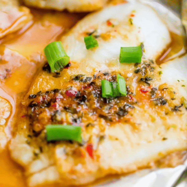 Close-up of Spicy Garlic Soy Baked Flounder fillet, topped with herbs, spices, and chopped green onions, served with a light sauce.