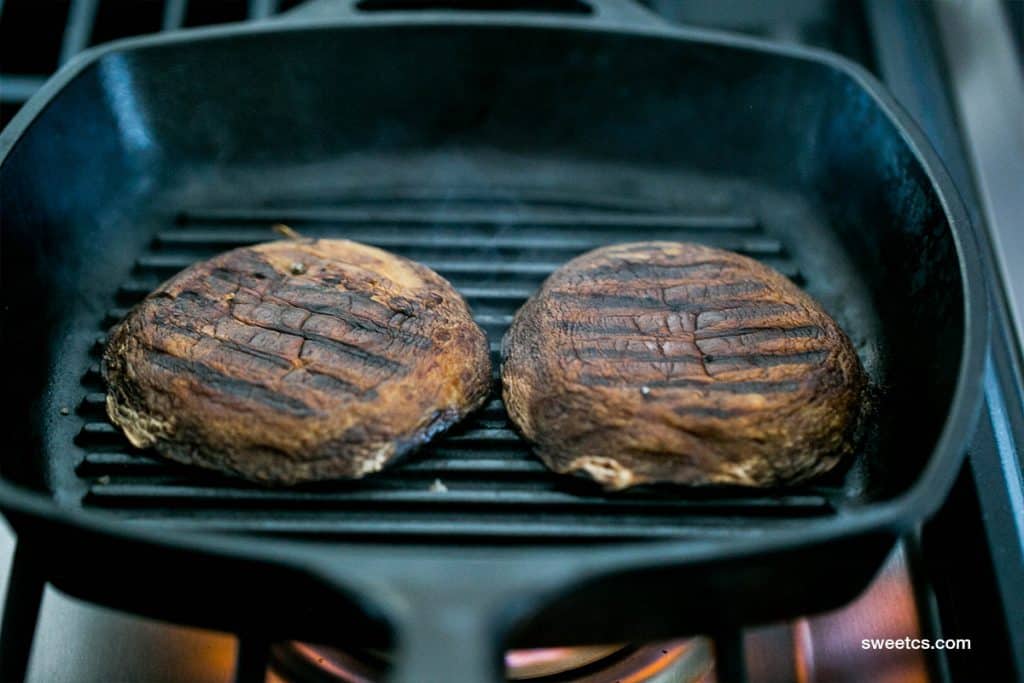 two scorched portobello mushrooms in a cast iron skillet 