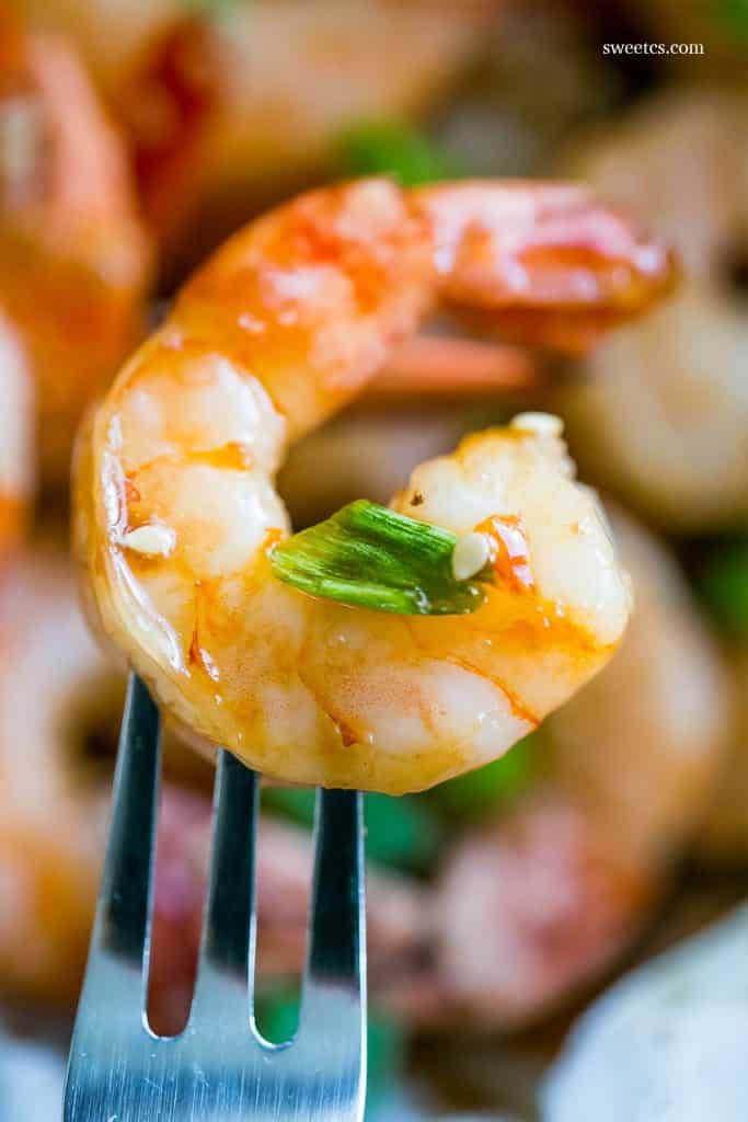 cooked shrimp with sesame seeds and green onions on them on a fork