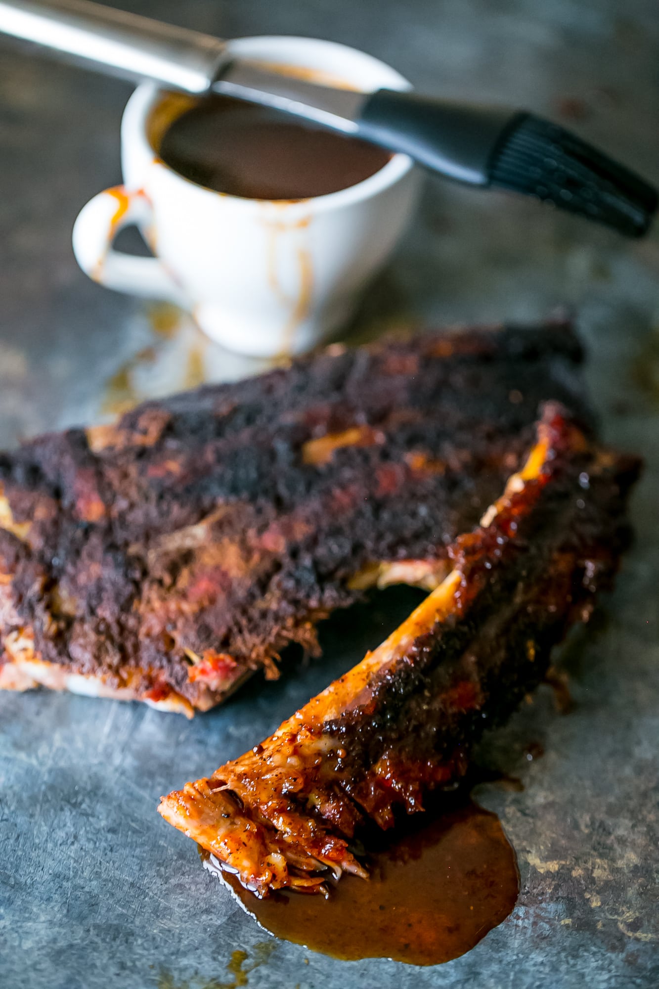 lovely fall off the bone ribs on a black surface with sauce in the background. 