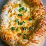 A Khachapuri Georgian Cheese Bread topped with green onions.