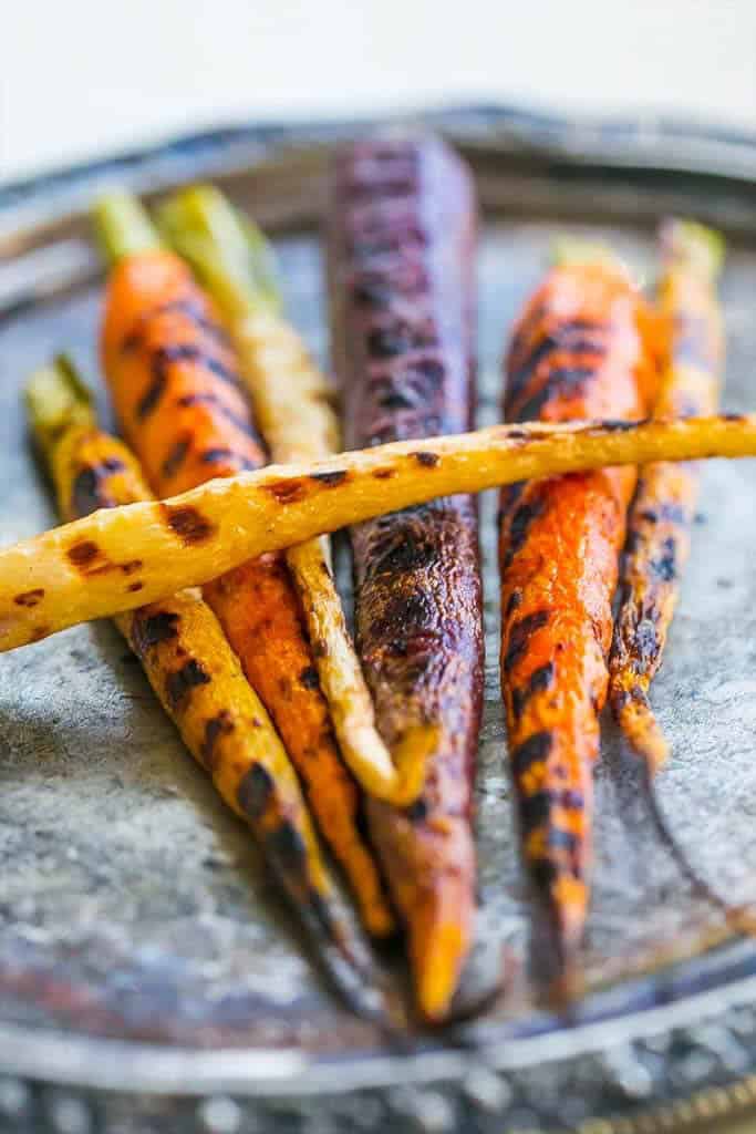 Pan roasted butter carrots, vibrant and multicolored, are beautifully arranged on a round metal plate.