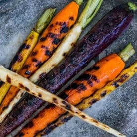 Pan roasted butter carrots and parsnips with charred marks are artfully arranged on a gray surface, showcasing their vibrant, earthy hues.