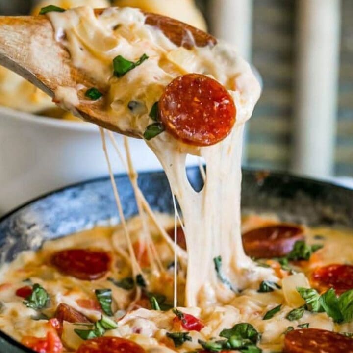 Cheesy spoon dipping into pepperoni dip.