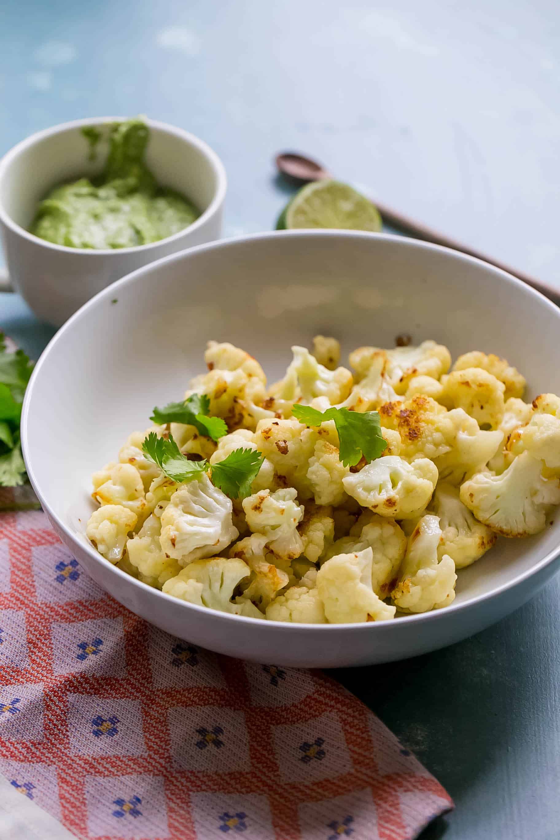 cauliflower in a bowl with pesto in a cup behind it on a table 