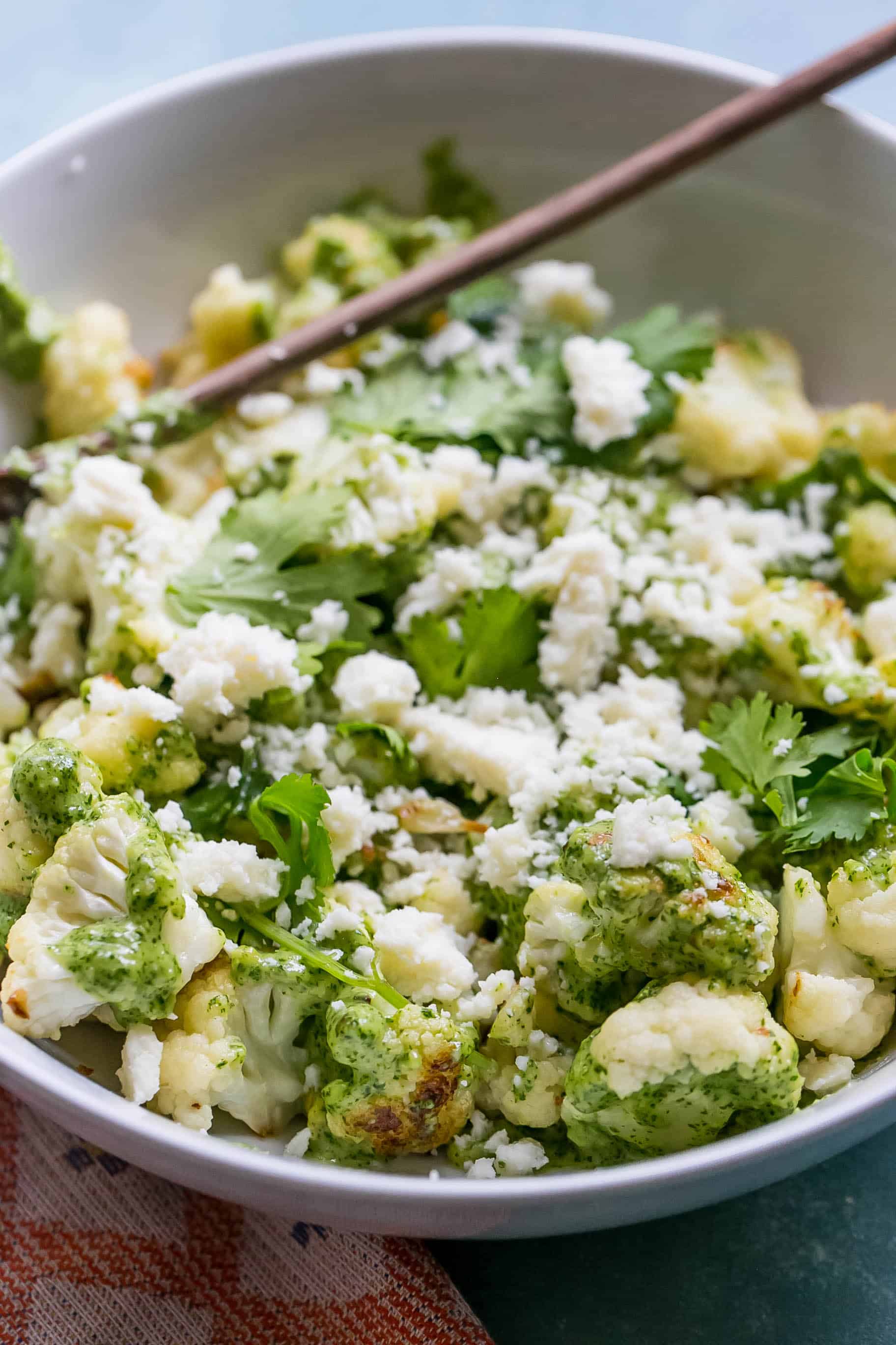 white bowl with cauliflower covered in pesto sauce and topped with crumbled white cheese