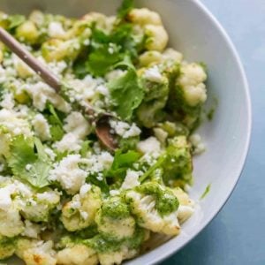 Roasted Cauliflower with Cilantro Cashew Pesto in a white bowl with a small wooden spoon