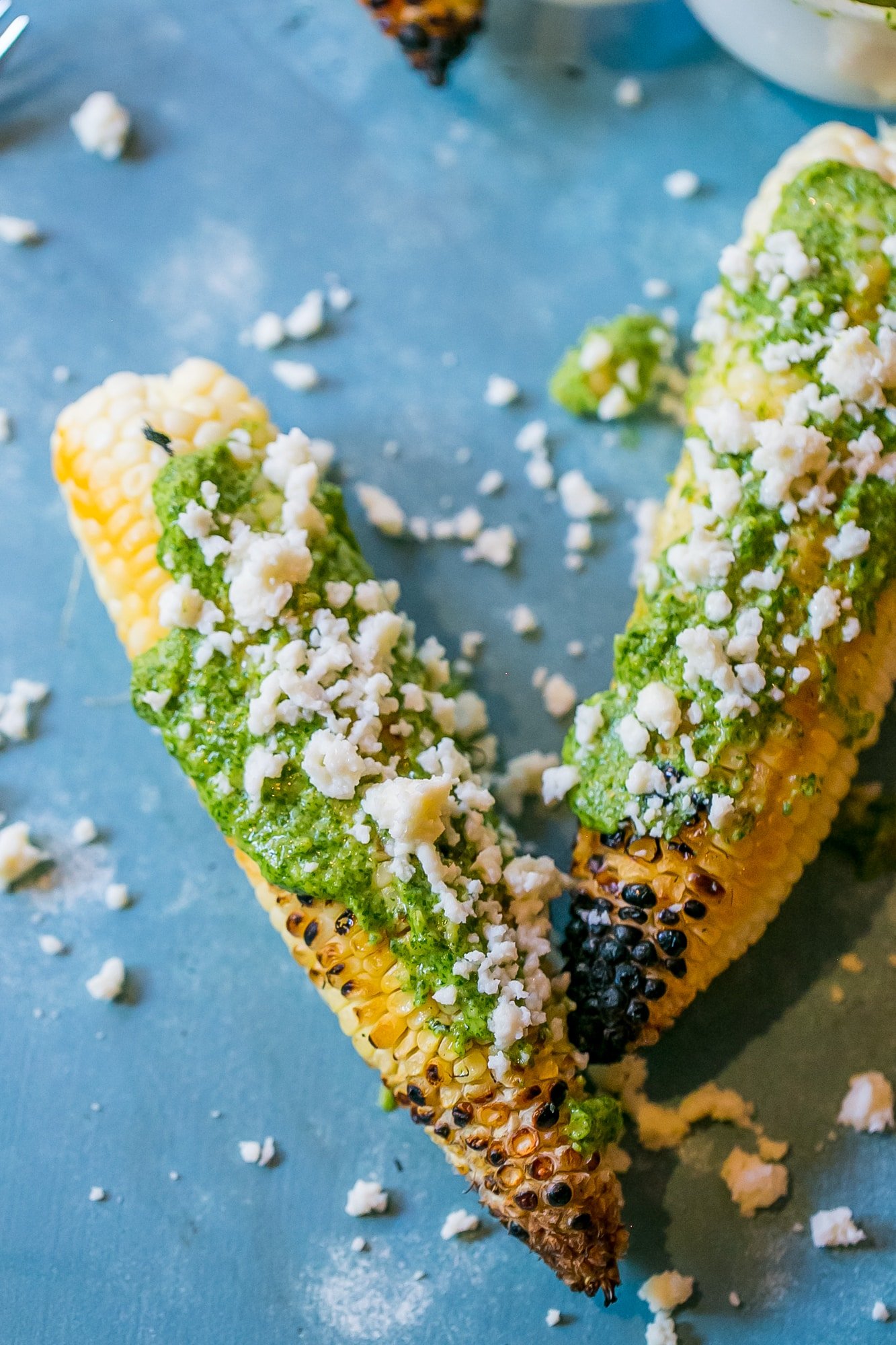 grilled corn with green pesto and crumbled cheese on it