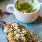 Grilled chicken topped with cashew cilantro pesto served on a blue plate.