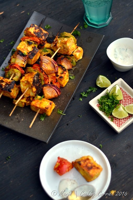 paneer and vegetable skewers on a platter with limes and cilantro around it