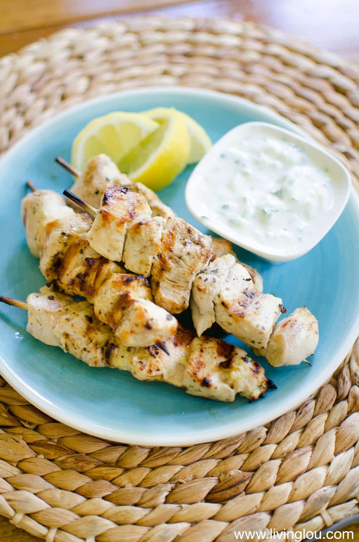 grilled chicken on a stick on a plate with creamy sauce and lemon