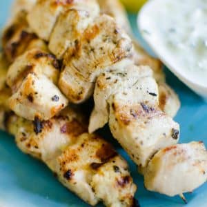 Greek chicken souvlaki with tzatziki sauce served on a blue plate.