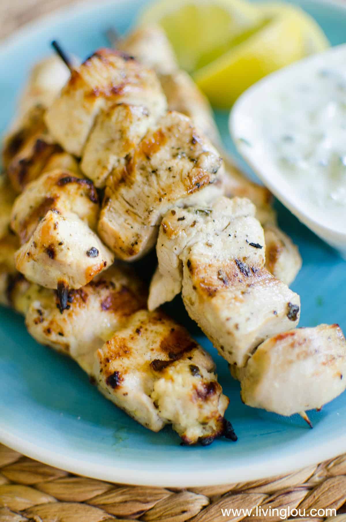 grilled chicken on a stick on a plate with creamy sauce and lemon