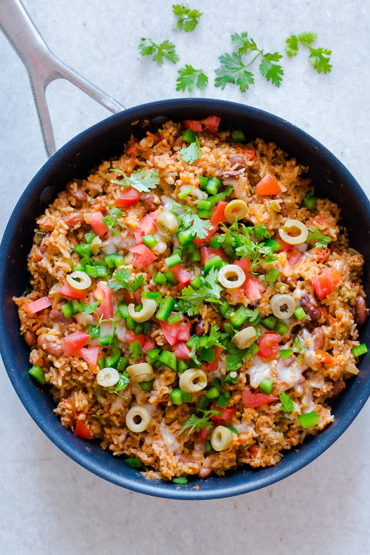 skillet with beef and rice, salsa, cilantro, jalapeno, and olives.