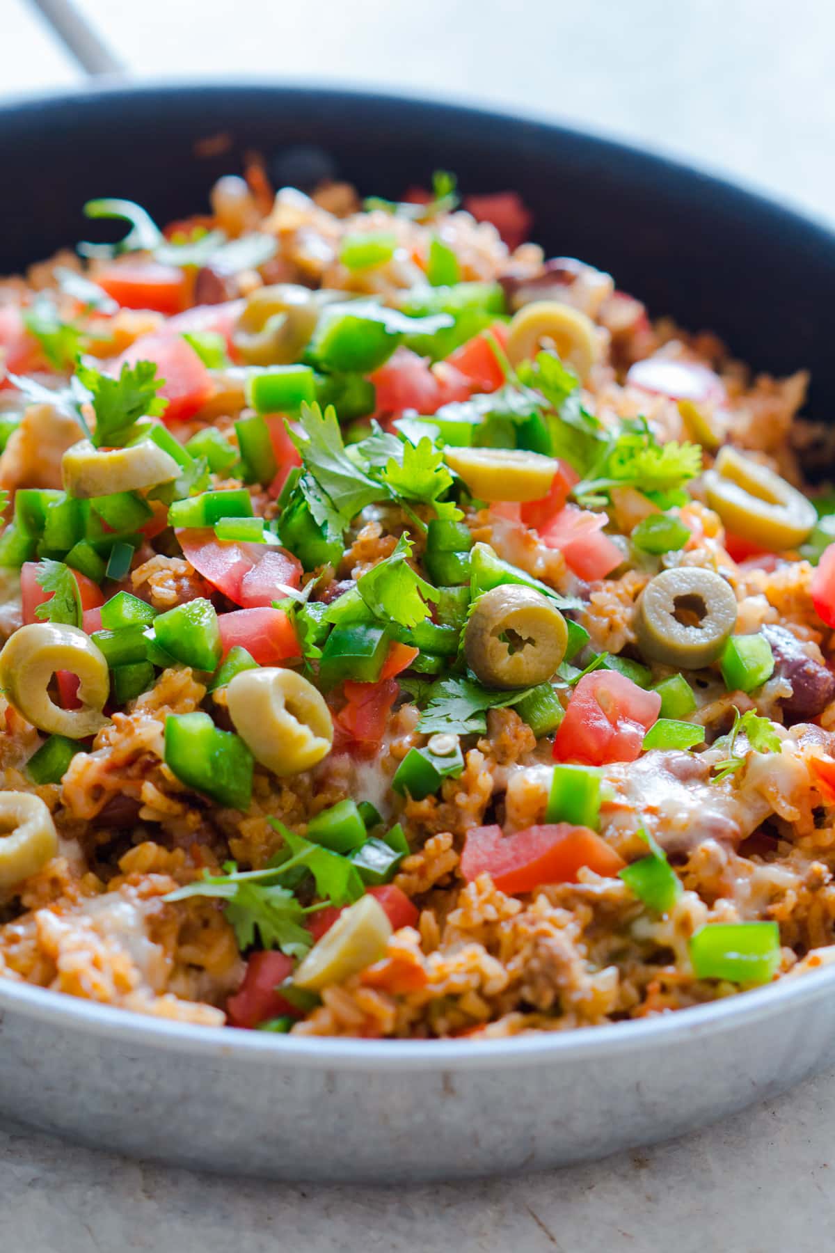 skillet with beef and rice, salsa, cilantro, jalapeno, and olives.