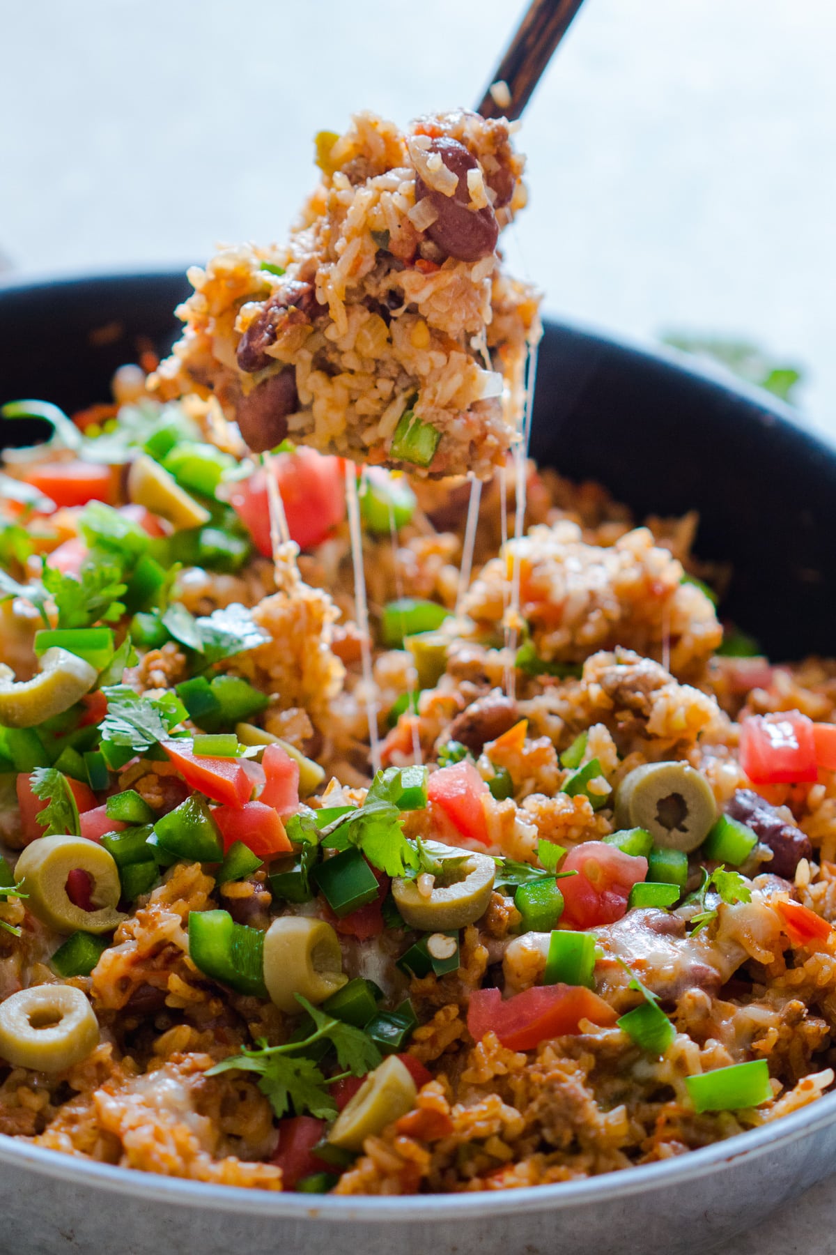 skillet with beef and rice, salsa, cilantro, jalapeno, and olives fork coming out of it all cheesy