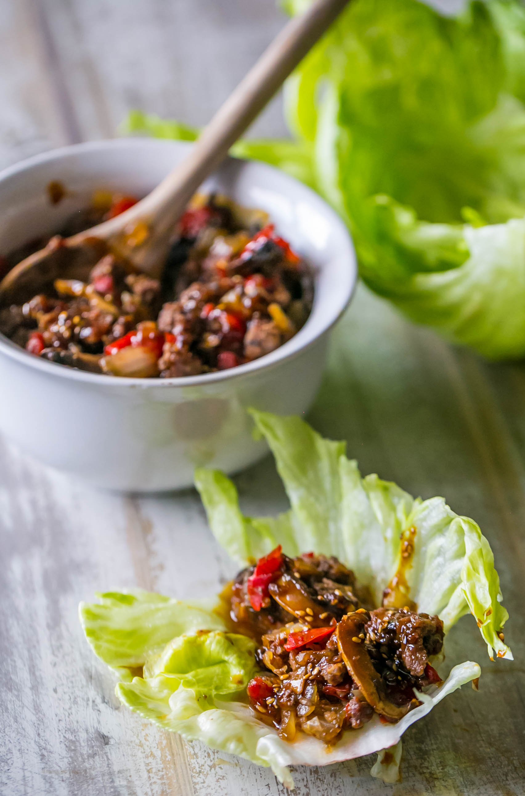 sweet chili beef and mushrooms in a lettuce wrap with sesame seeds on it with sweet chili beef in a bowl in the background