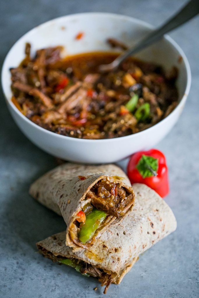 Slow Cooker Sweet Chili Soy Shredded Pork wrapped in a whole wheat tortilla with a bowl of shredded pork in the background 