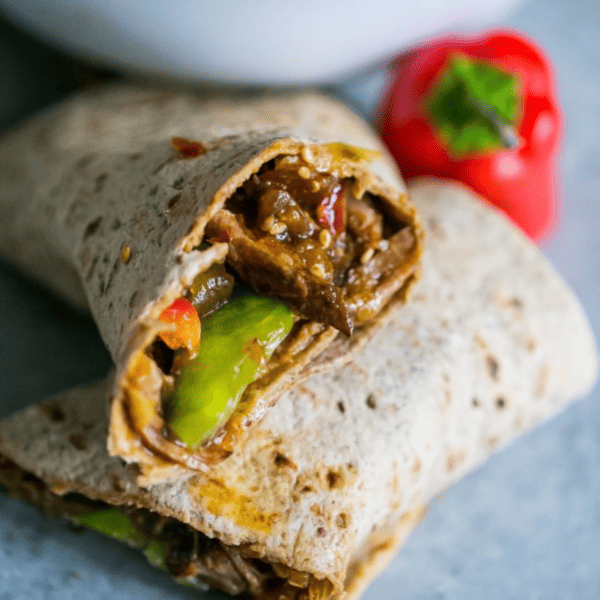A burrito with sweet chili shredded pork and peppers on a plate.