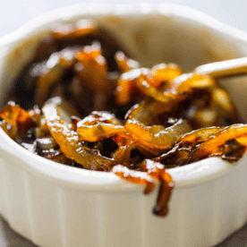 A white ramekin filled with honey whiskey caramelized onions, with a utensil partially visible on the right side.