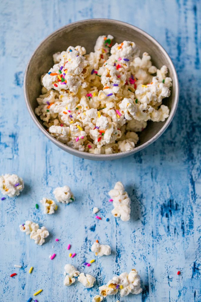 bowl of popcorn covered in white chocolate with colorful sprinkles on it