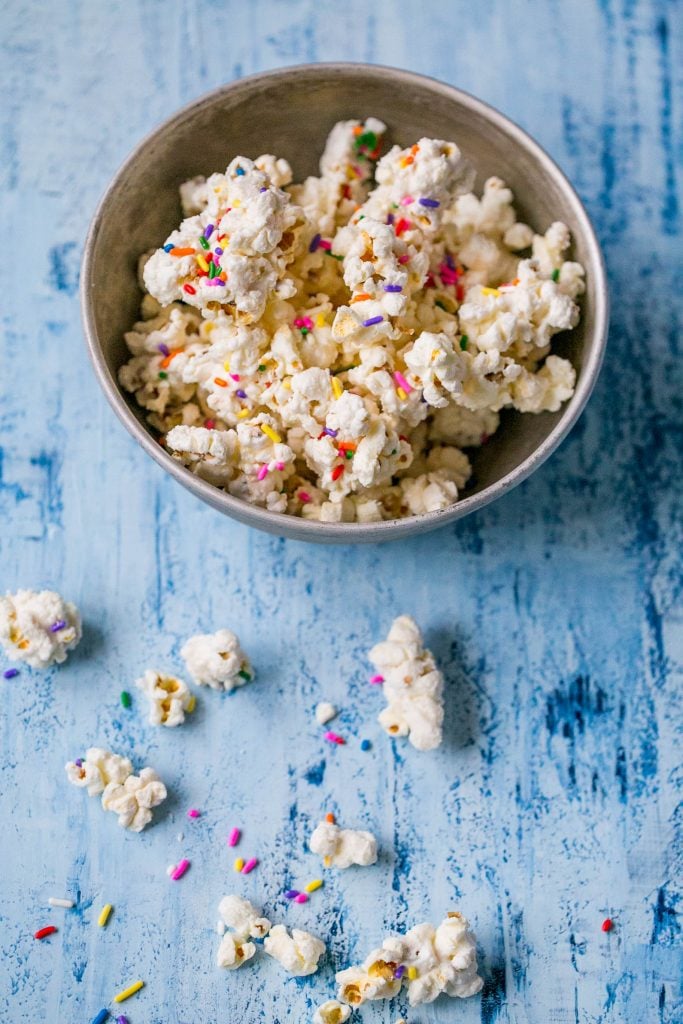 bowl of popcorn covered in white chocolate with colorful sprinkles on it