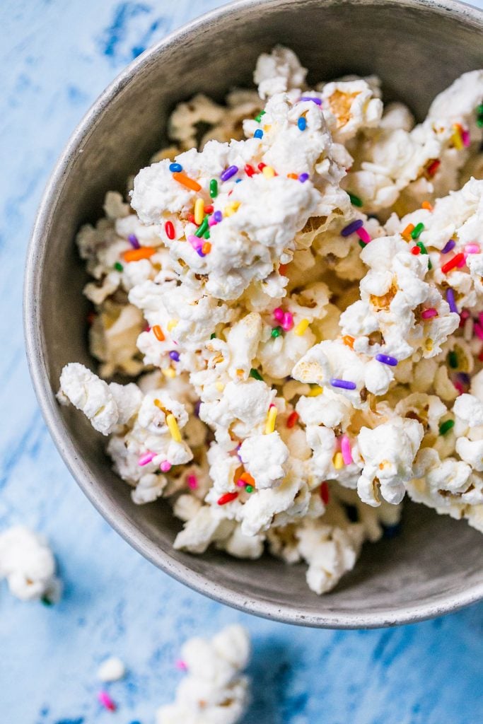 bowl of popcorn covered in white chocolate with colorful sprinkles on it