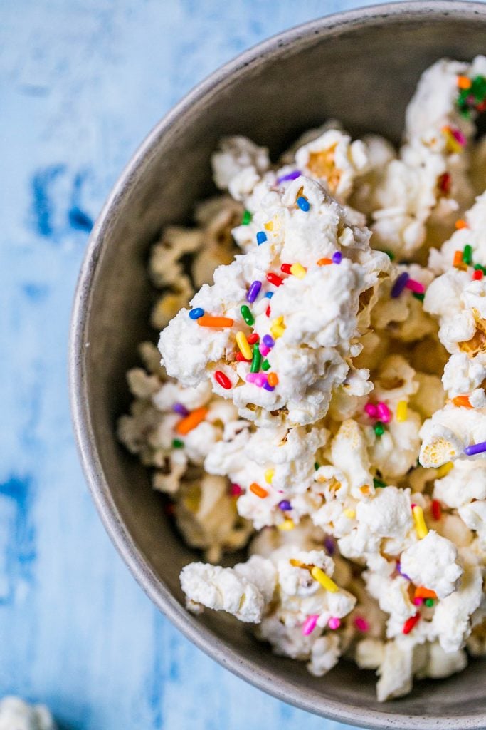 bowl of popcorn covered in white chocolate with colorful sprinkles on it