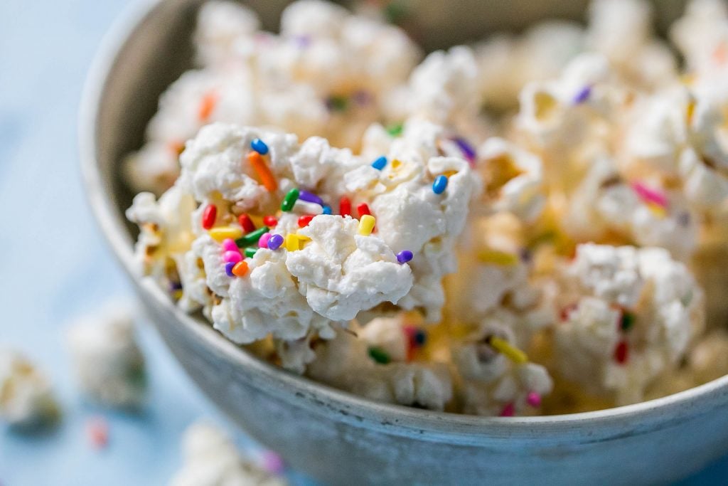 bowl of popcorn covered in white chocolate with colorful sprinkles on it