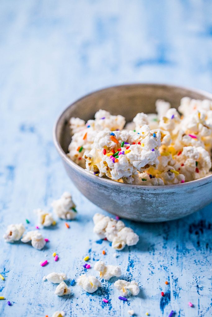 bowl of popcorn covered in white chocolate with colorful sprinkles on it